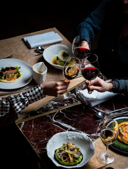 Des personnes trinquent avec leurs verres de vin au-dessus d’une table où des plats sont disposés