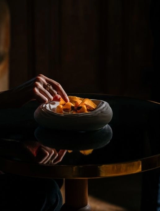Plan d'une main atteignant un bol avec de la nourriture disposée de manière épurée.