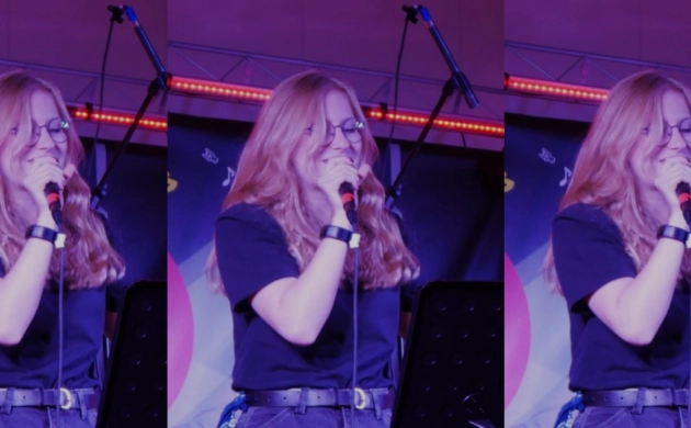 Nina, jeune musicienne, chante sur scène, un micro à la main, sur un fond tamisé éclairée par des néons violet et rouge