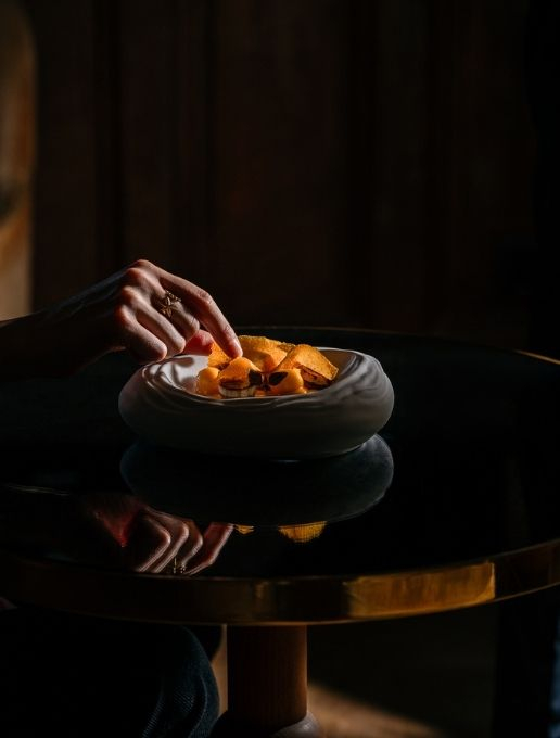 Plan d'une main atteignant un bol avec de la nourriture disposée de manière épurée.