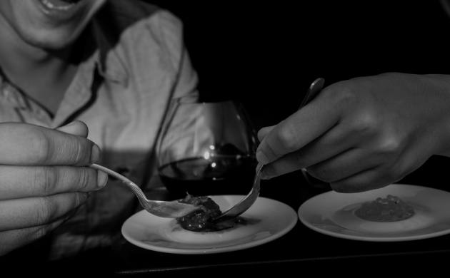 Deux personnes dégustent des petites portions de plats dans le noir, mettant leurs sens à l’épreuve lors d’une expérience sensorielle.